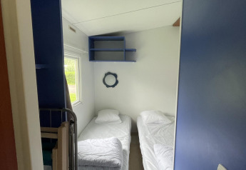 Pequeño dormitorio en Cottage Zen, Camping Seasonova Vesoul, Francia, con dos camas individuales y estantes azules.