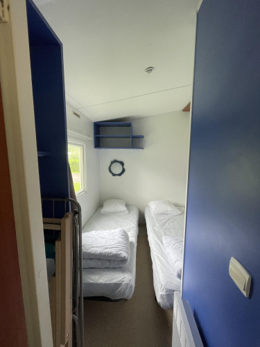 Pequeño dormitorio en Cottage Zen, Camping Seasonova Vesoul, Francia, con dos camas individuales y estantes azules.