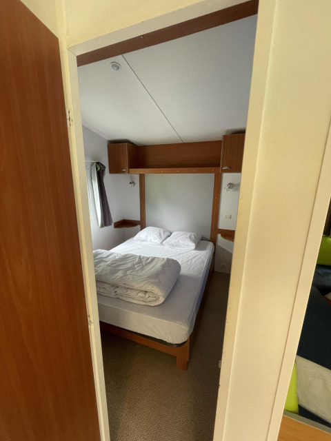 Doorkijk naar een gezellige slaapkamer met tweepersoonsbed in Cottage Zen, Camping Seasonova Vesoul, Frankrijk.