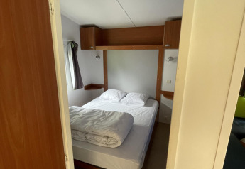Doorkijk naar een gezellige slaapkamer met tweepersoonsbed in Cottage Zen, Camping Seasonova Vesoul, Frankrijk.