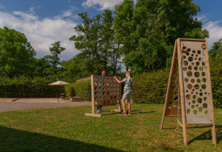 To mennesker spiller et stort udendørs brætspil i en grøn park på Camping Seasonova Vittel i Frankrig.