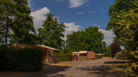 Houten chalets en weelderig groen op Camping Seasonova Vittel, een vakantiepark in Grand Est, Frankrijk bij zonnig weer.