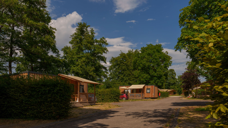 Wooden cabins and lush greenery at Camping Seasonova Vittel holiday park in Grand Est, France on a sunny day.