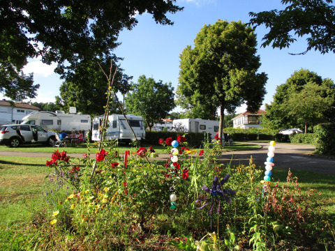 Camping Seasonova Vittel in Grand Est, France, with motorhomes, lush flowers, and trees on a sunny day.