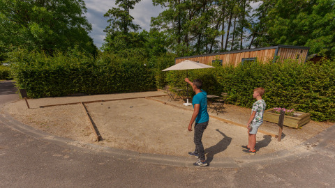 Twee mensen spelen petanque op een zandveld aan Camping Seasonova Vittel, midden in het groen.