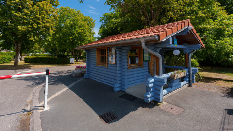 Cabaña de madera azul en la entrada de Camping Seasonova Vittel, rodeada de árboles, Grand Est, Francia.
