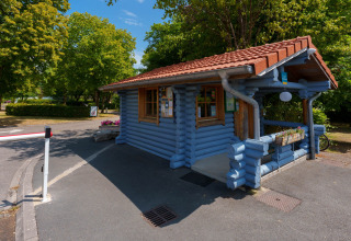 Blå træhytte ved indgangen til Camping Seasonova Vittel, omgivet af træer, Grand Est, Frankrig.