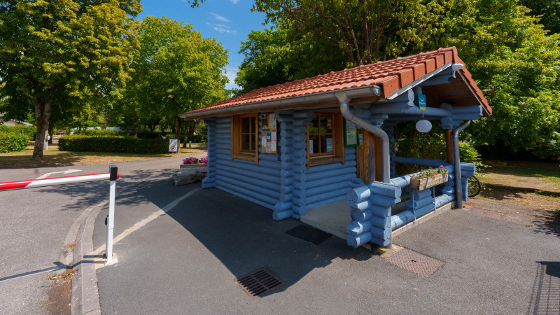 Blue wooden cabin at the entrance of Camping Seasonova Vittel, surrounded by trees, Grand Est, France.