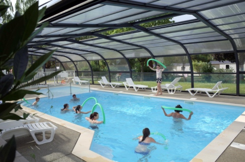 Covered swimming pool at Camping Seasonova Les Portes d'Alsace with guests enjoying water activities and pool noodles.