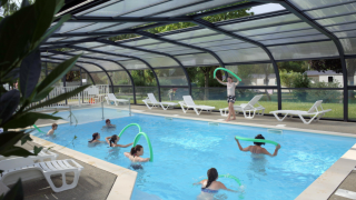 Piscina cubierta en Camping Seasonova Les Portes d'Alsace con personas disfrutando actividades acuáticas y flotadores.