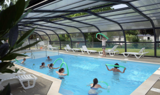 Piscina cubierta en Camping Seasonova Les Portes d'Alsace con personas disfrutando actividades acuáticas y flotadores.
