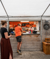 Puesto de comida al aire libre con clientes y personal en Camping Seasonova Les Portes d'Alsace, Grand Est, Francia.