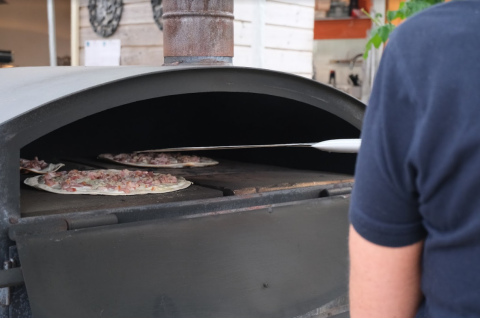 Una persona hornea pizzas en un gran horno de piedra en Camping Seasonova Les Portes d'Alsace, Grand Est, Francia.