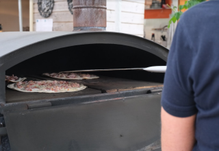 Eine Person backt Pizzen in einem großen Steinofen im Camping Seasonova Les Portes d'Alsace, Grand Est, Frankreich.