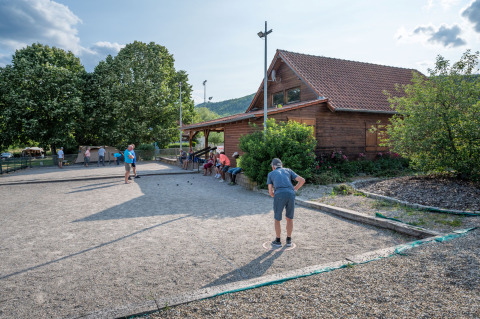 Menschen spielen Boule auf einem Kiesplatz vor einer Holzhütte im Camping Seasonova Les Portes d'Alsace in Frankreich.