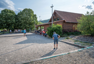 Menschen spielen Boule auf einem Kiesplatz vor einer Holzhütte im Camping Seasonova Les Portes d'Alsace in Frankreich.