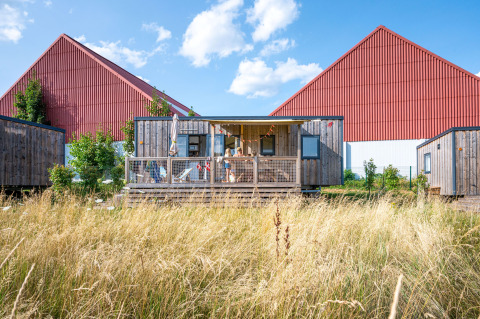 Houten chalet tussen hoog gras bij Camping Seasonova Les Portes d'Alsace, vakantiepark in Grand Est, Frankrijk.