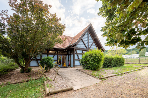 Wood-framed house with a red roof surrounded by greenery at Camping Seasonova Les Portes d'Alsace, Grand Est, France.