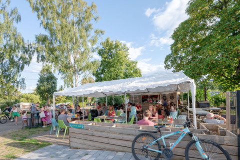 People relax at an outdoor café under a marquee at Camping Seasonova Les Portes d'Alsace, surrounded by trees.