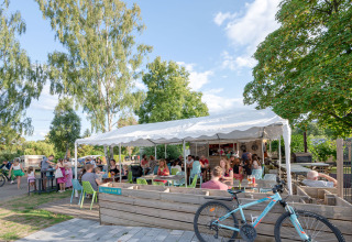 Des gens profitent d'une terrasse couverte au Camping Seasonova Les Portes d'Alsace, entourés d'arbres verdoyants.