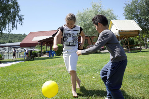 Dos niños juegan con una pelota amarilla sobre el césped en Camping Seasonova Les Portes d'Alsace, Grand Est, Francia.