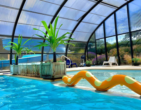 Indoor swimming pool with slide, tropical plants and lounge chairs at Camping Seasonova Etennemare in Normandy.
