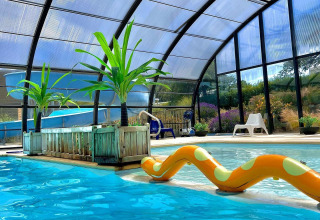 Indoor swimming pool with slide, tropical plants and lounge chairs at Camping Seasonova Etennemare in Normandy.