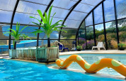 Indendørs swimmingpool med gennemsigtig overdækning, glider, planter og solsenge på Camping Seasonova Etennemare.