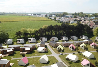 Aerial view of Camping Seasonova Etennemare in Normandy, France, showing cabins, tents, and open fields.