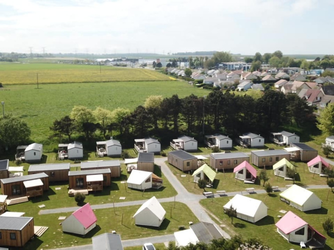 Aerial view of Camping Seasonova Etennemare in Normandy, France, showing cabins, tents, and open fields.