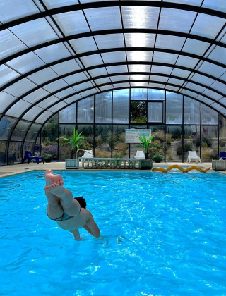 Persona saltando a una piscina cubierta en Camping Seasonova Etennemare, un parque vacacional en Normandía, Francia.