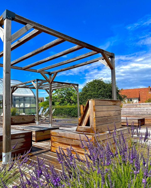 Espace glamping extérieur avec terrasse en bois, bancs, lavande en fleurs et ciel bleu éclatant.