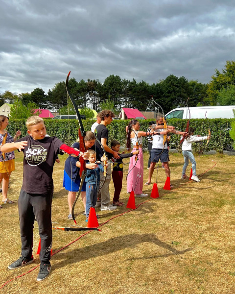 Niños y adultos practican tiro con arco en una zona verde junto a tiendas safari en Camping Seasonova Etennemare.