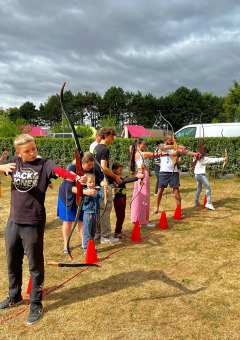 Niños y adultos practican tiro con arco en una zona verde junto a tiendas safari en Camping Seasonova Etennemare.