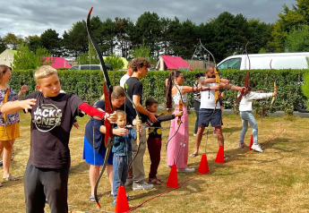 Niños y adultos practican tiro con arco en una zona verde junto a tiendas safari en Camping Seasonova Etennemare.