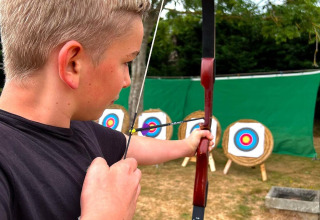 Blonde jongen richt met pijl en boog op doelen op Camping Seasonova Etennemare, Normandië, Frankrijk.