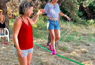 Vrouw helpt een meisje balanceren op een slackline bij Camping Seasonova Etennemare in Normandië, Frankrijk.