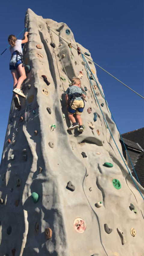 Dos niños escalan un muro de escalada al aire libre bajo un cielo azul en Camping Seasonova Etennemare, Normandía.