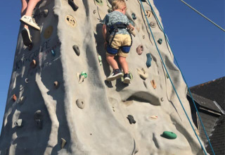 Two children climbing a tall outdoor climbing wall under a blue sky at Camping Seasonova Etennemare, Normandy.