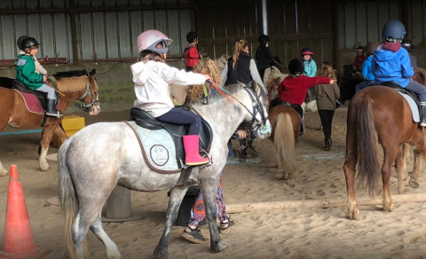 Niños participan en una clase de equitación en recinto cubierto en Camping Seasonova Etennemare en Normandía, Francia.