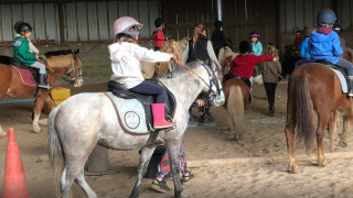 Niños participan en una clase de equitación en recinto cubierto en Camping Seasonova Etennemare en Normandía, Francia.