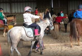 Niños participan en una clase de equitación en recinto cubierto en Camping Seasonova Etennemare en Normandía, Francia.