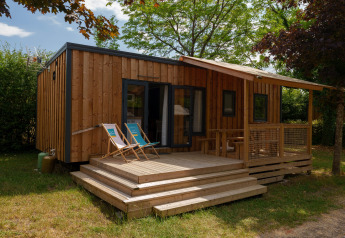 Houten lodge met terras en twee ligstoelen, omringd door bomen in een groene en rustige omgeving.