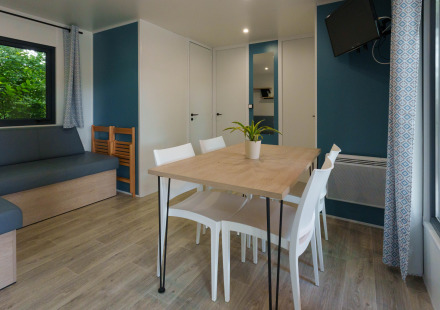 Moderne lodge woonkamer met eettafel, witte stoelen, hoekbank, wand-tv en grote ramen met gordijnen.