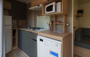 Cocina compacta en lodge con estufa, microondas, lavavajillas, nevera, utensilios y sofá gris.
