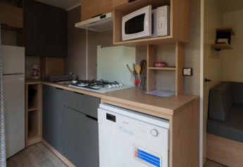 Compacte lodgekeuken met gaskookplaat, microgolfoven, vaatwasmachine, ijskast en zitbank.