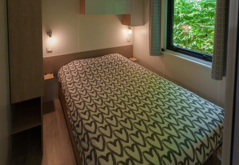 Gezellige lodge slaapkamer met tweepersoonsbed, hartjesdeken en raam met zicht op het groen buiten.