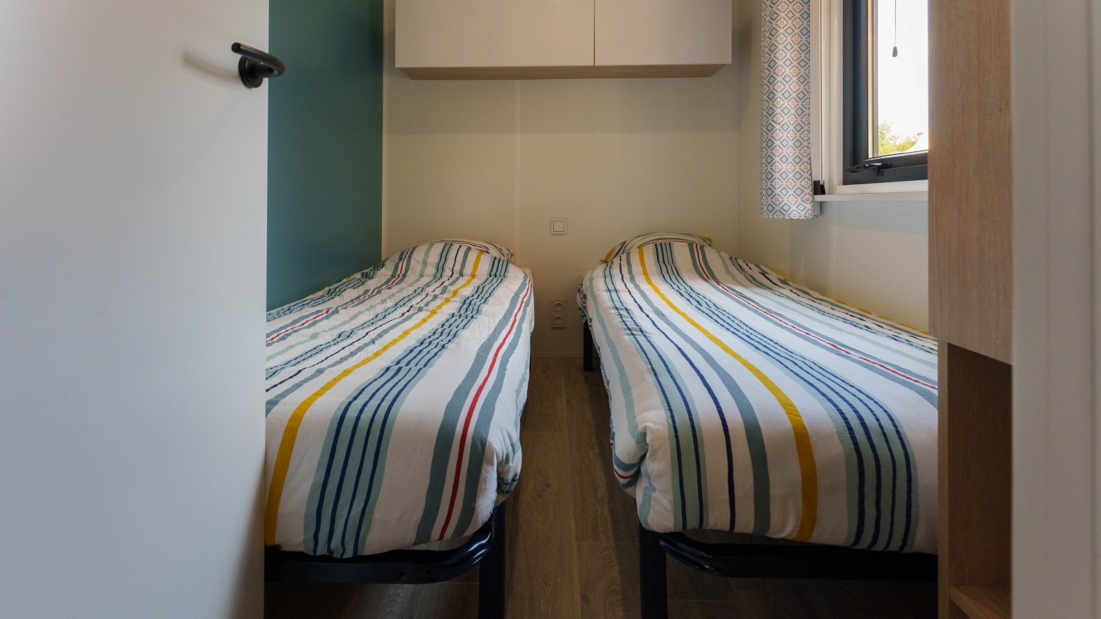 Kleine slaapkamer in een lodge met twee eenpersoonsbedden, gestreept beddengoed, raam en wandkasten.