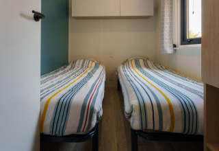 Et lille værelse i en lodge med to enkeltsenge dækket af stribede dyner, vindue og væghængte skabe.