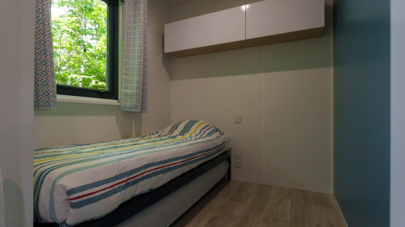 Bright single bedroom with patterned curtains, window, and overhead storage in a cozy lodge setting.